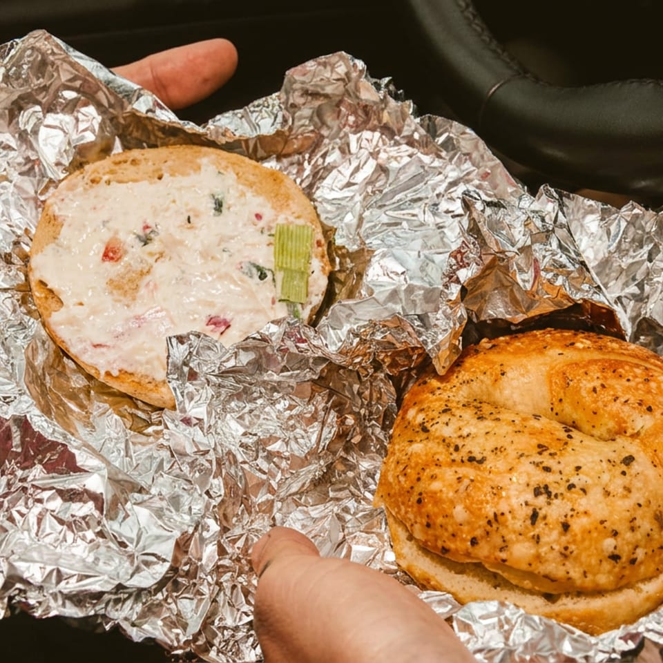 Two bagels, one with cream cheese and celery, wrapped in foil and held in a car.