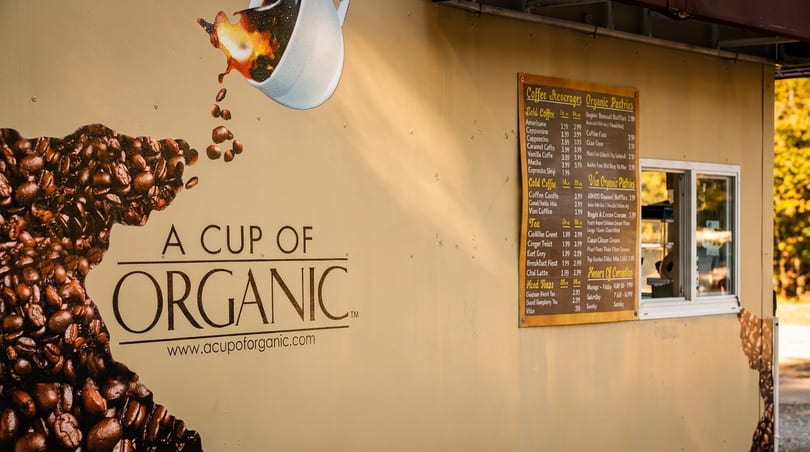 A Cup of Organic coffee stand with a large coffee bean graphic, menu board, and service window.